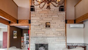 A cozy living area with a stone fireplace, two armchairs, a wooden coffee table, and a chandelier. - Quality Inn near Rocky Mountain National Park (Estes Park)