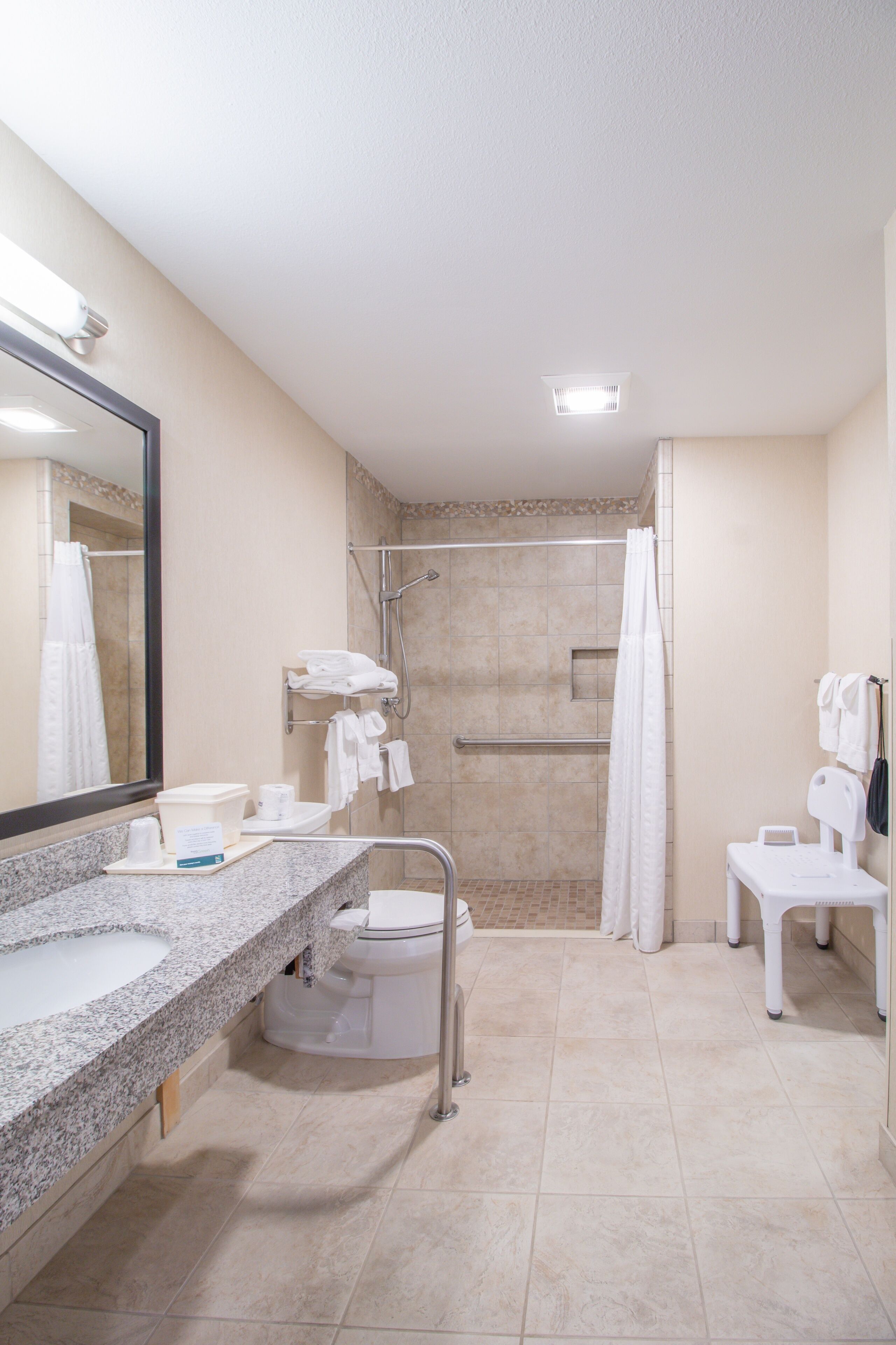 A modern bathroom with a granite countertop, a toilet, a shower stall, and a vanity with a mirror.