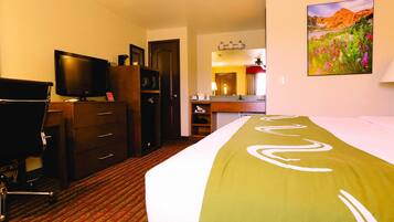Una camera d'albergo con un letto, una scrivania con un computer, una televisione, un armadio e un bagno visibile attraverso una porta aperta.