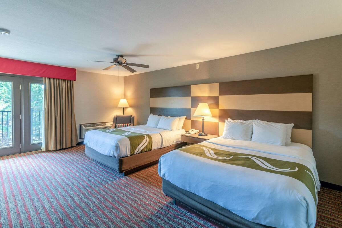Habitació d'hotel amb dos llits, un ventilador de sostre, una finestra gran amb cortines i un disseny de paret a quadres.