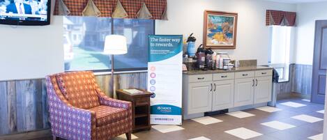 A reception area with a patterned armchair, a television, a banner, and a kitchen counter.