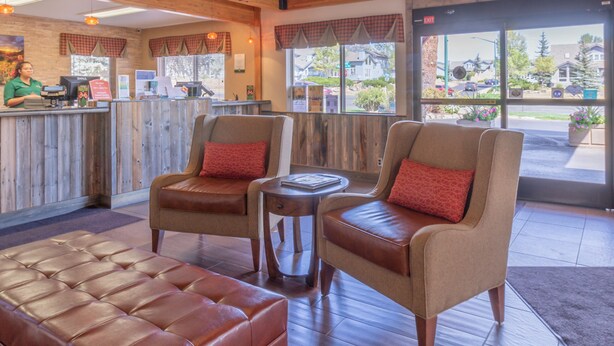 A lobby with a wooden ceiling, a chandelier, two armchairs with red cushions, a leather ottoman, and a reception desk. - Quality Inn near Rocky Mountain National Park (Estes Park)