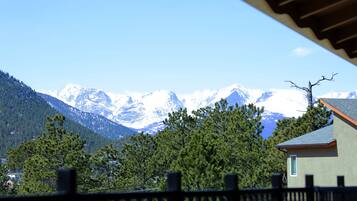 A mountain landscape with snow-capped peaks, a house with a sloped roof, and a wooden fence in the foreground.