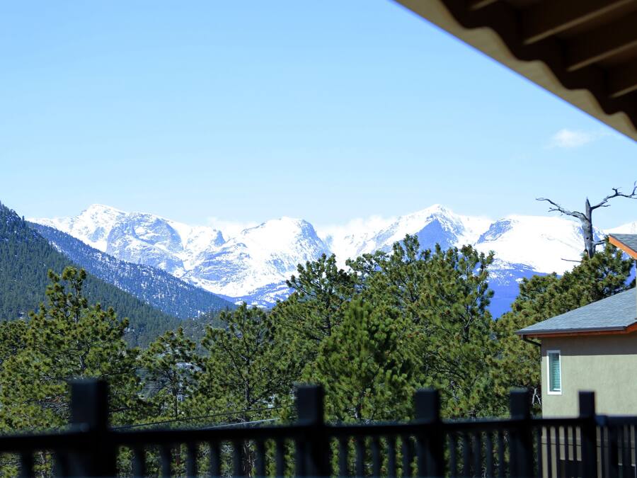 A mountain landscape with snow-capped peaks, a house with a sloped roof, and a wooden fence in the foreground.