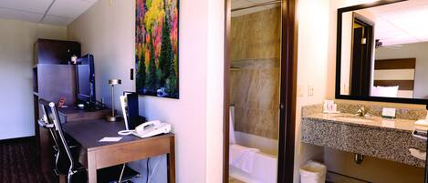 Habitación de hotel con escritorio, silla, ordenador y un cuadro en la pared.