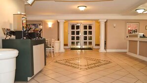 A reception area with a tiled floor, a reception desk, and a set of double doors leading to another room. - The Grand by Capital O Texarkana I-30 (Texarkana)