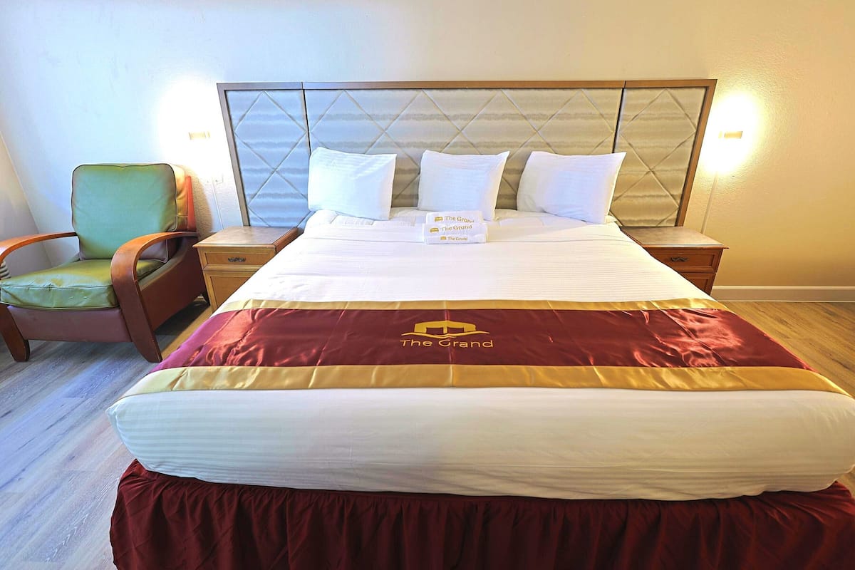 Quarto de hotel com uma cama grande, uma mesa de cabeceira, uma cadeira e cabeceira com padrão de losangos.