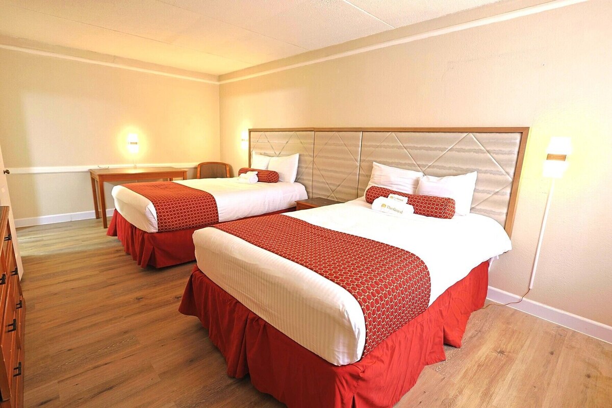 A hotel room with two beds, wooden flooring, and a headboard with a geometric pattern.