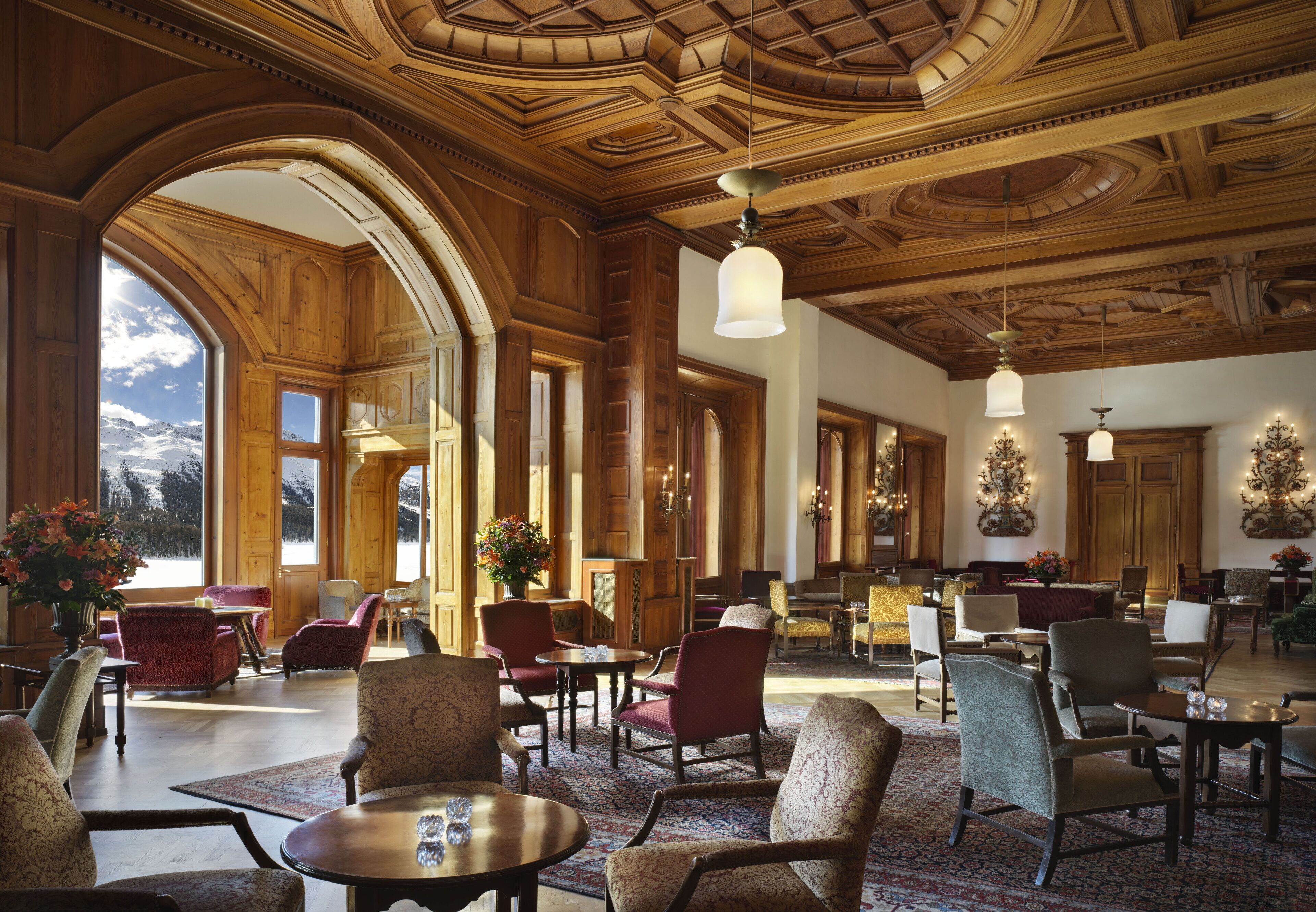 A spacious lobby with wooden paneling, large arched windows, and a variety of seating arrangements.