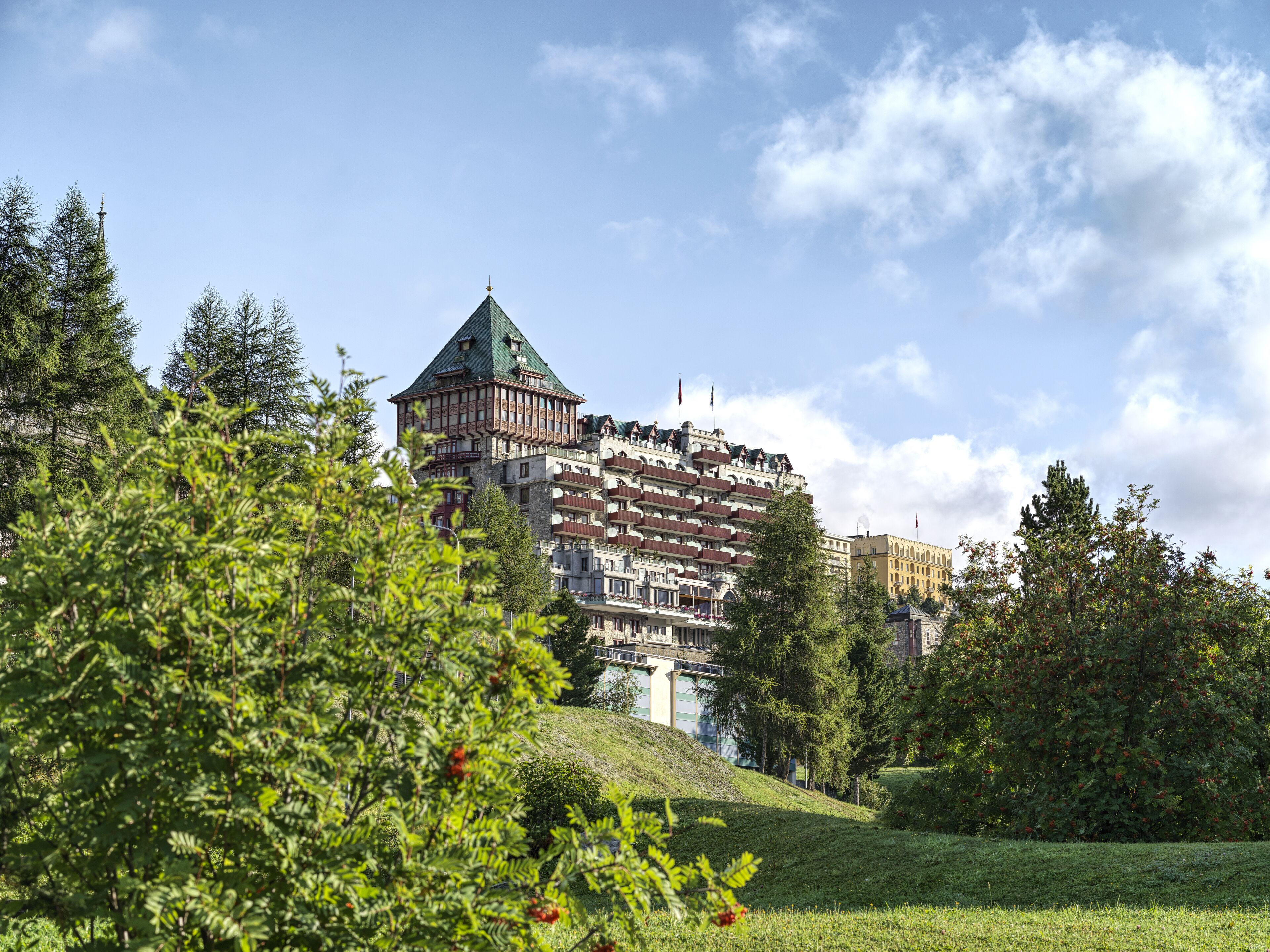 A multi-story hotel with a prominent tower and a green roof, surrounded by lush greenery and trees.