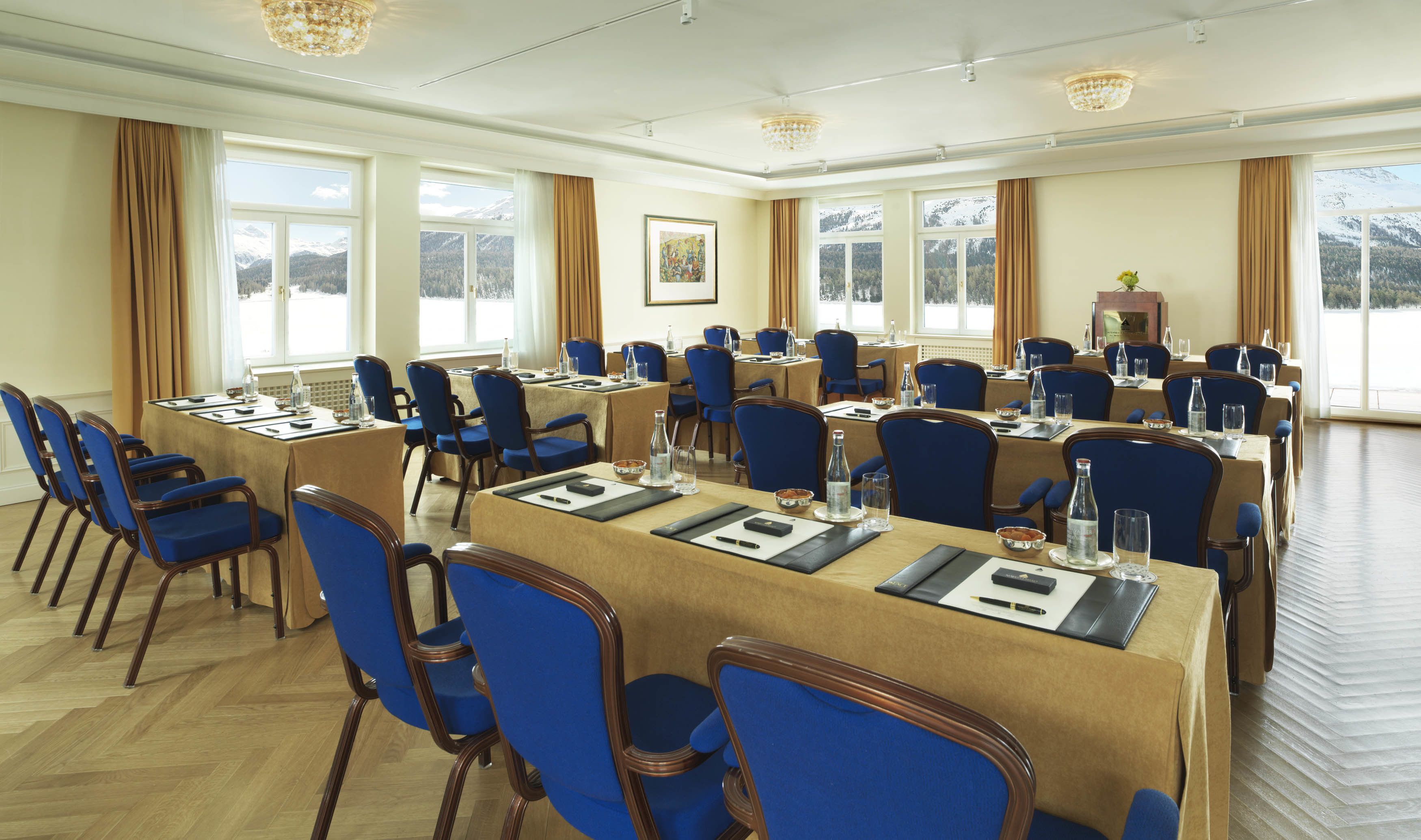Une salle de conférence dotée de plusieurs tables et chaises, de grandes fenêtres offrant une vue sur des montagnes enneigées et d’un lustre.
