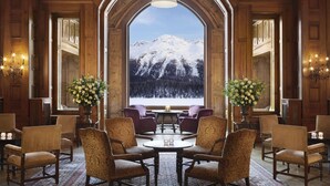 A grand lobby with a large arched window offering a view of a snow-covered mountain. - Badrutt's Palace Hotel (St. Moritz)