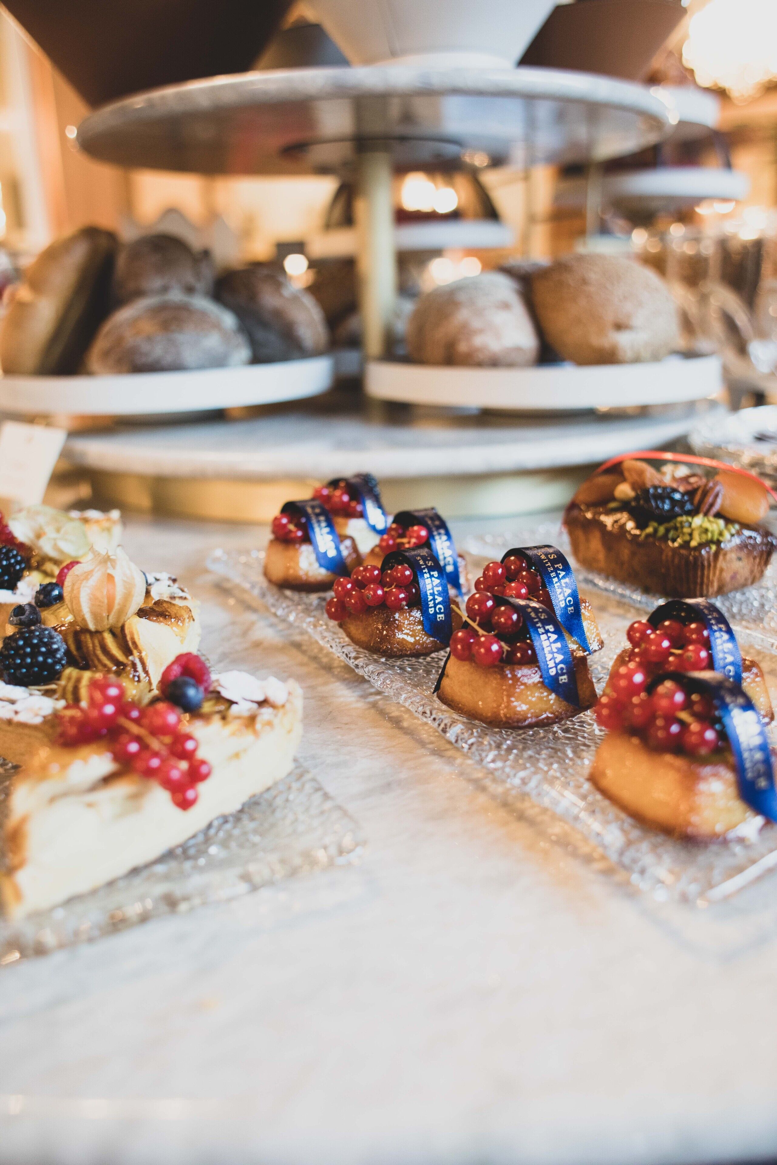 A variety of pastries and desserts on display, including cakes and tarts, with some garnished with berries and ribbons.