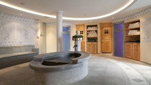A modern lobby with a central stone fountain, wooden cabinets, and a decorative wall with architectural drawings.