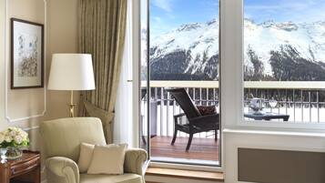 A room with a view of snow-covered mountains, a chair, a lamp, and a vase of flowers.