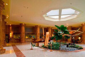 A lobby with marble flooring, large wooden columns, a reception desk, and a tropical plant arrangement.