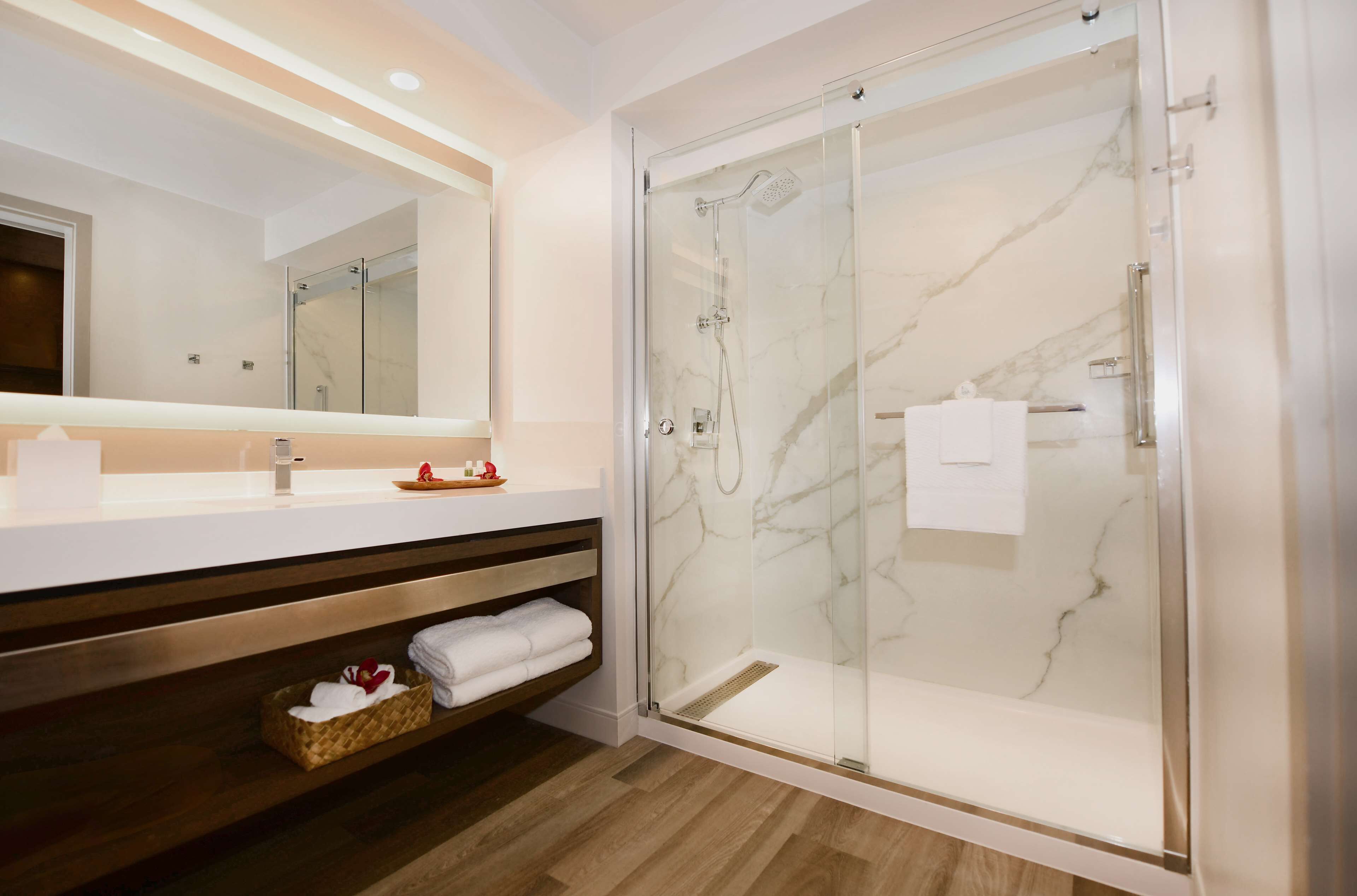 Une salle de bain moderne avec une douche à parois de verre, un grand miroir et un meuble-lavabo en bois doté d’une étagère.