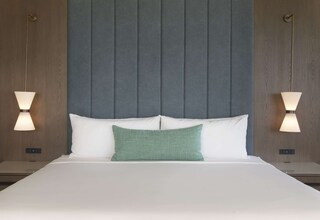 A hotel room with a large bed, two bedside tables, a green pillow, and wall-mounted lamps.