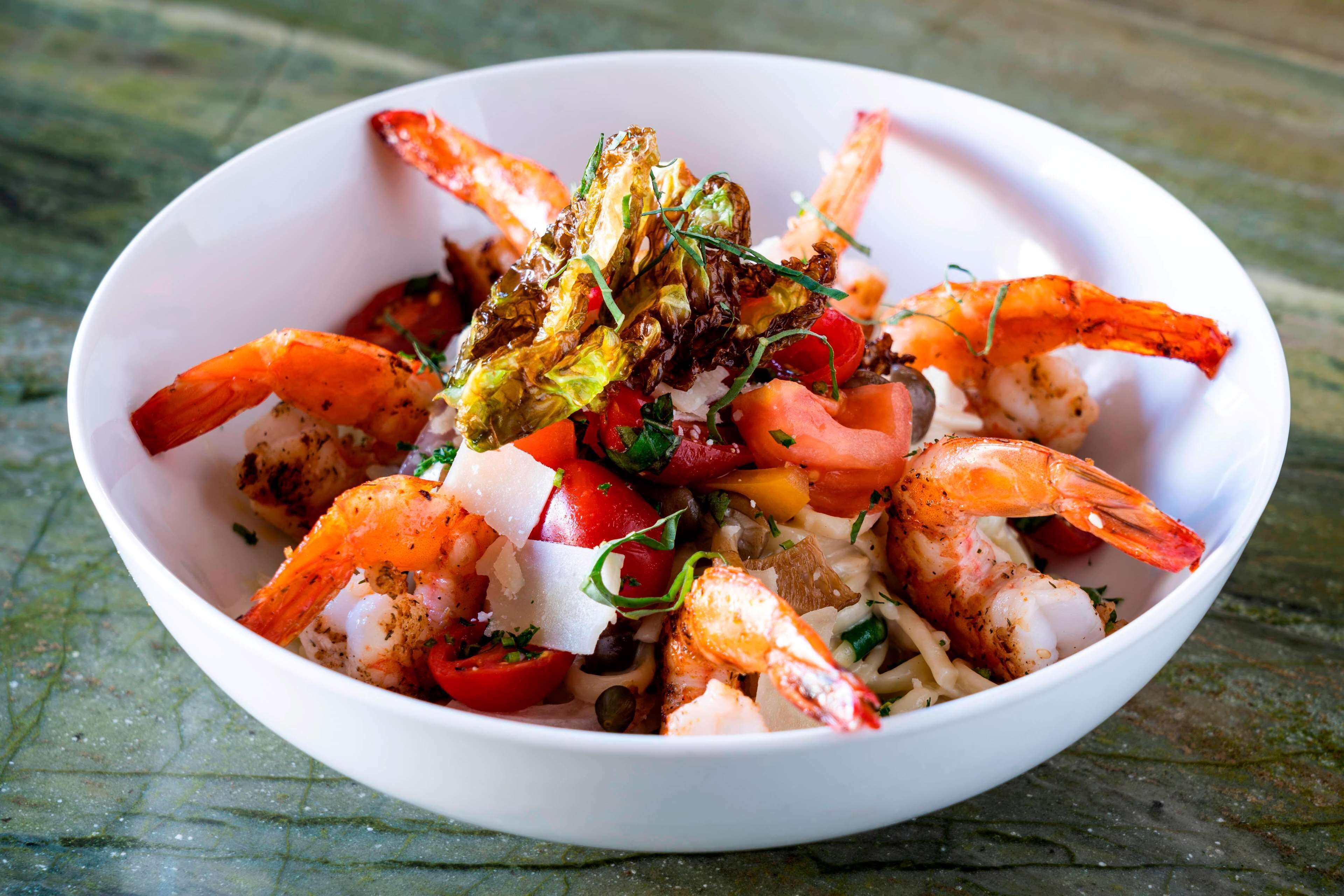 Un tazón de ensalada de camarones con lechuga, tomates y queso.