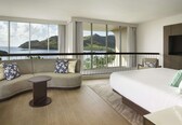 A hotel room with a large bed, a sofa, a small table, and a view of the ocean.