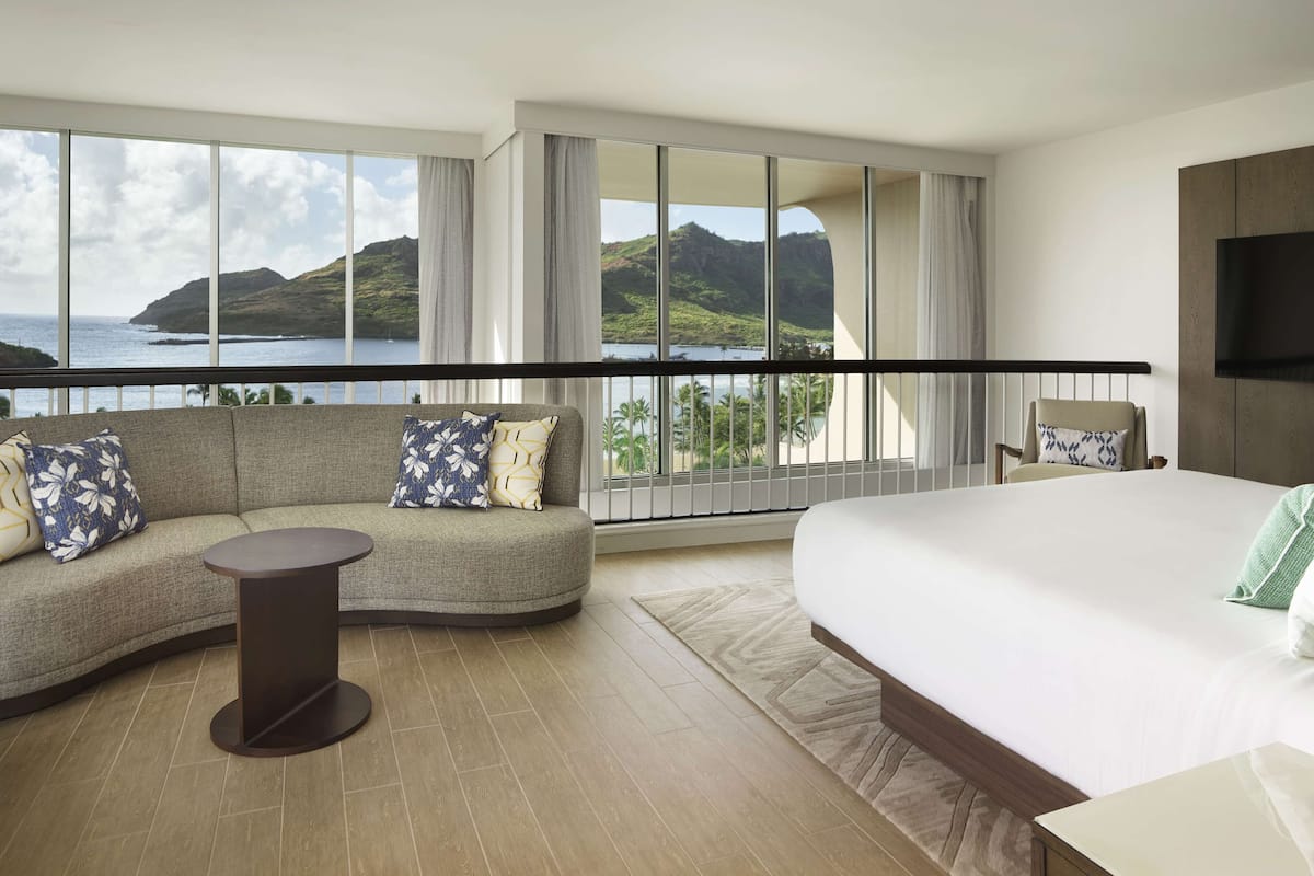 A hotel room with a large bed, a sofa, a small table, and a view of the ocean.