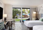 A hotel room with a bed, a desk, a chair, and a view of the outdoor pool area.