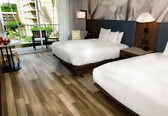 A hotel room with two beds, a small table with chairs, and a view of the outside balcony.