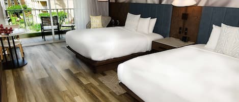 A hotel room with two beds, a small table with chairs, and a view of the outside balcony.