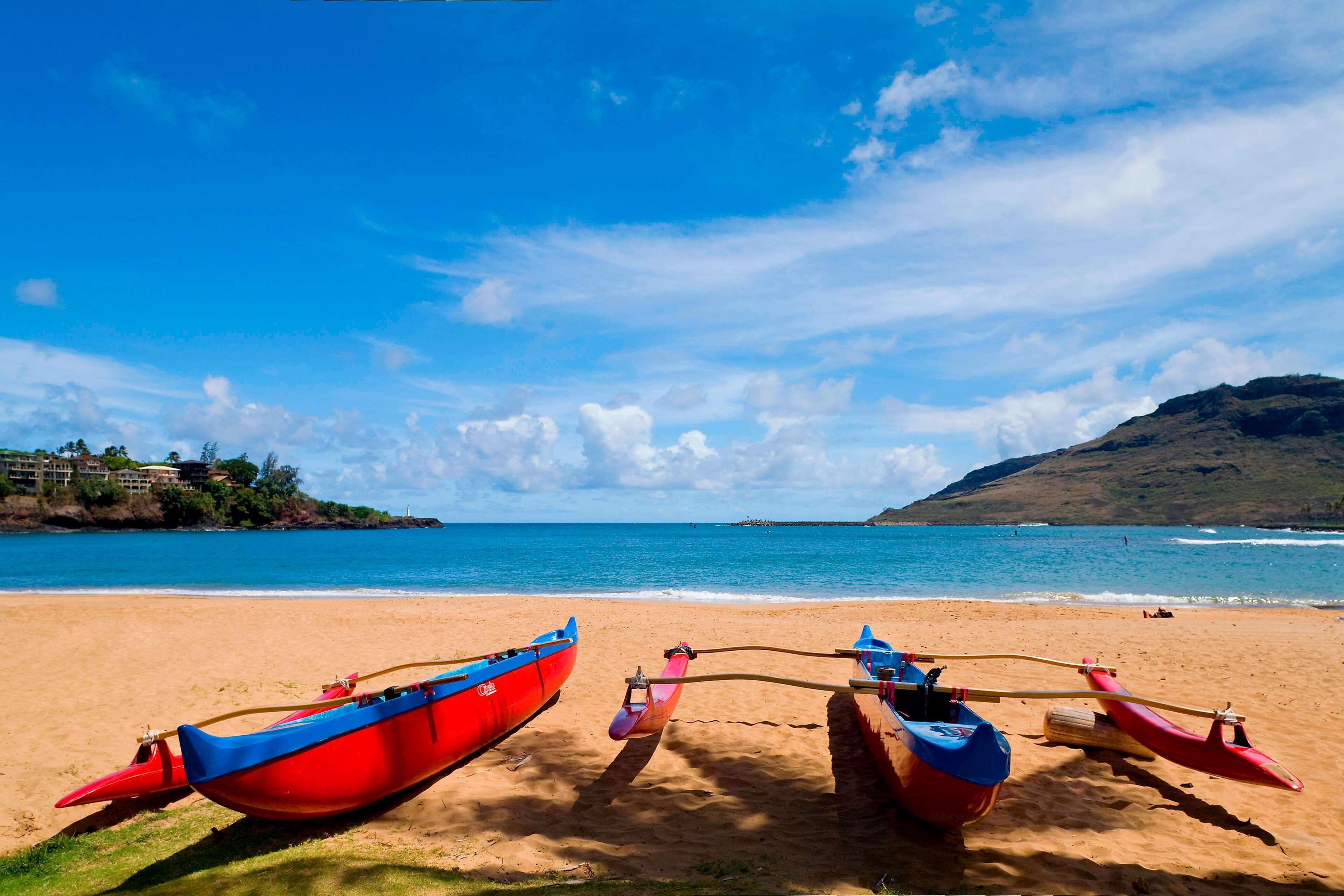 A beach with two red and blue boats tied to a wooden post.