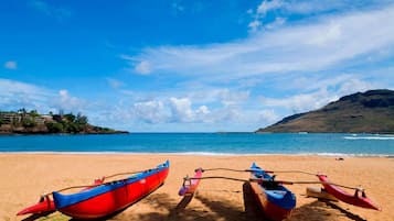 A beach with two red and blue boats tied to a wooden post.