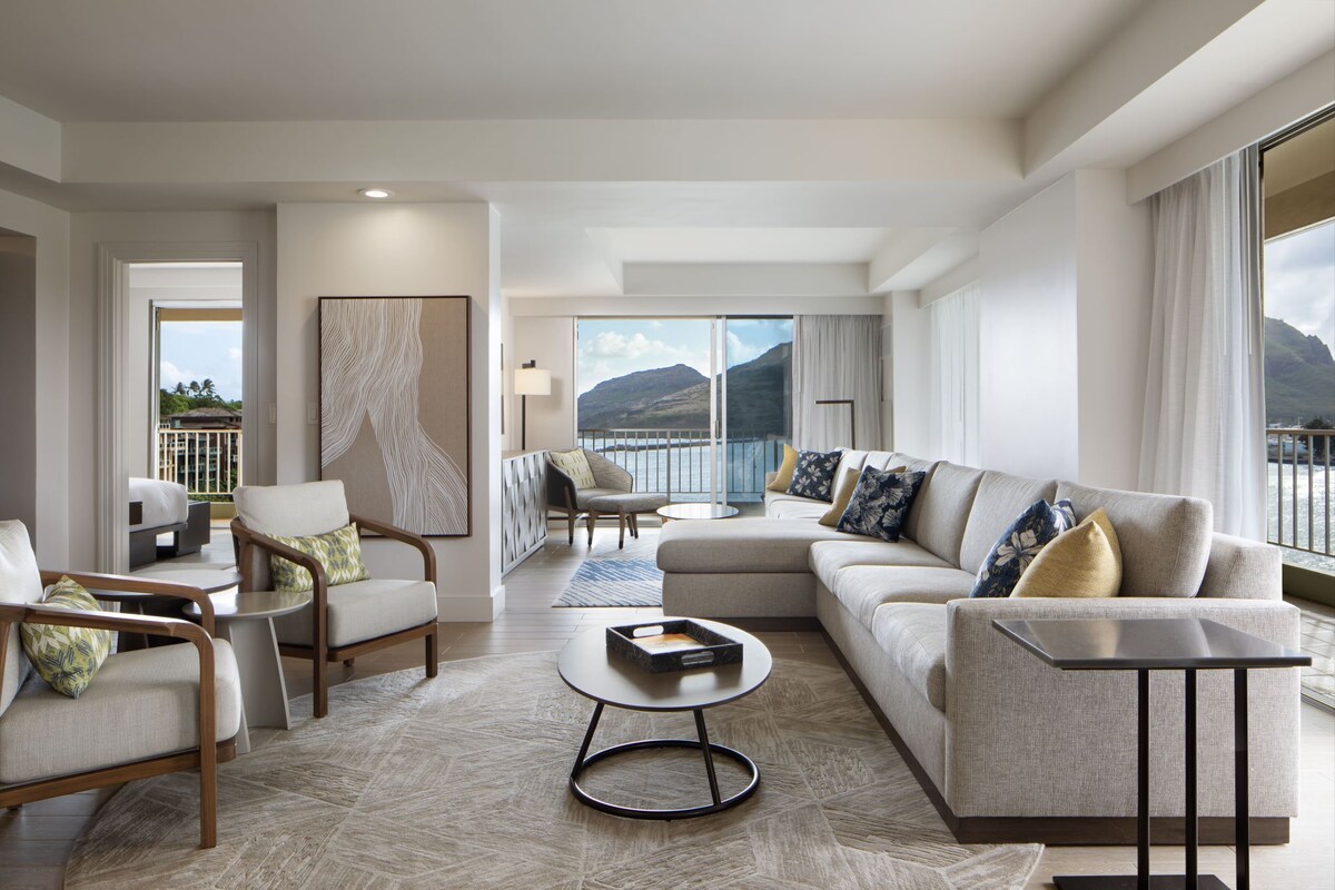 A modern living room with a sofa, chairs, a coffee table, and a view of a mountain and water.