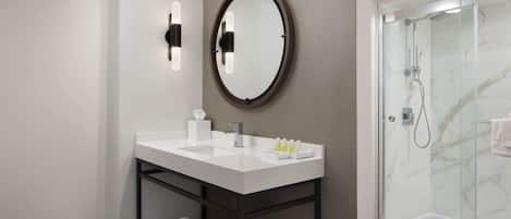 Un baño moderno con un tocador blanco, un espejo grande y una ducha con cerramiento de vidrio.