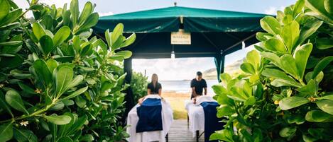 A wooden pathway leading to a massage tent with a sign, surrounded by lush greenery.