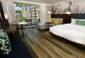 A hotel room with a large bed, a desk, a chair, and a view of a building through a window.