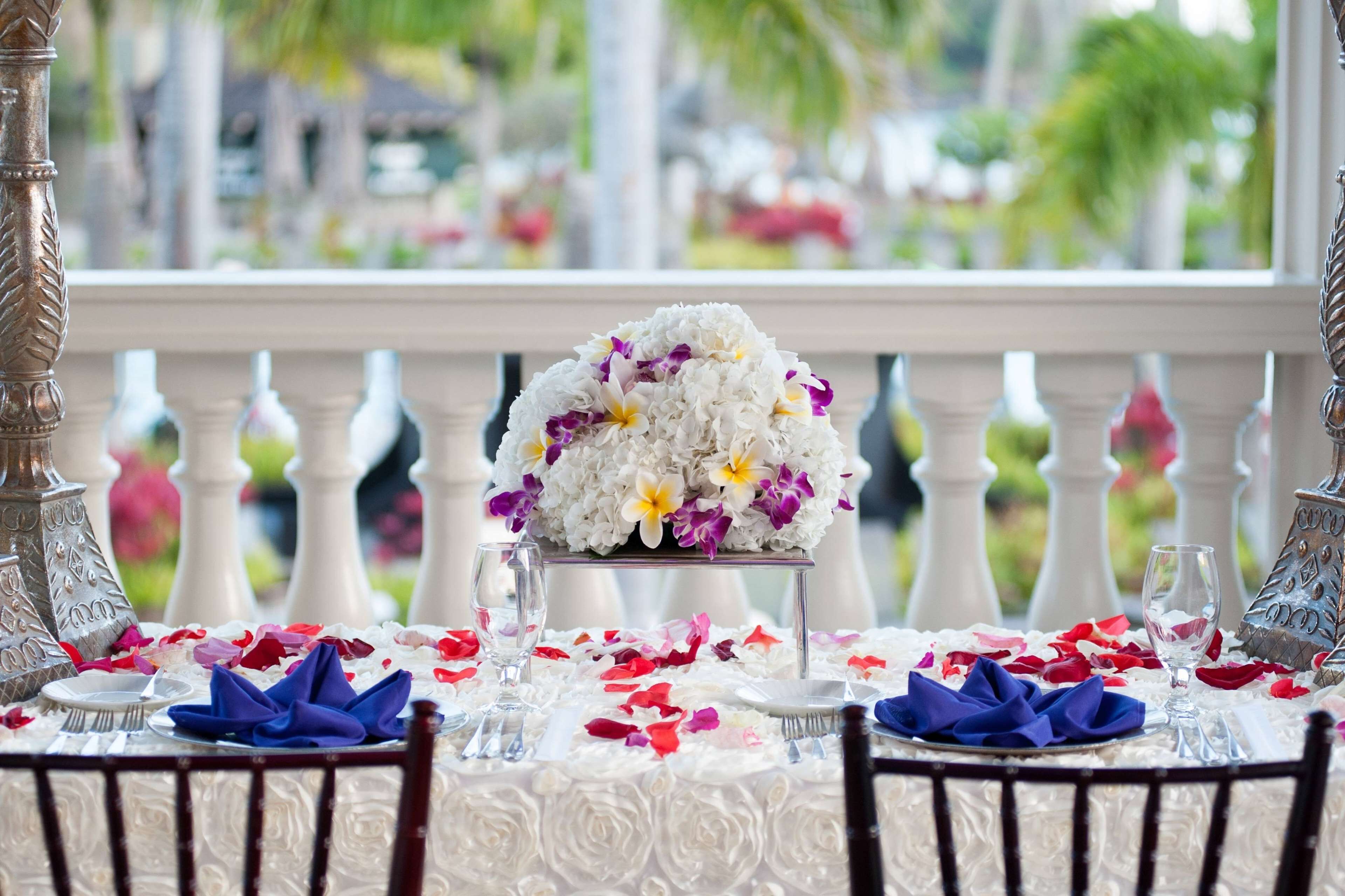 A table set for a meal with a floral centerpiece, white tablecloth, and a balcony view.