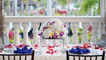 A table set for a meal with a floral centerpiece, white tablecloth, and a balcony view.