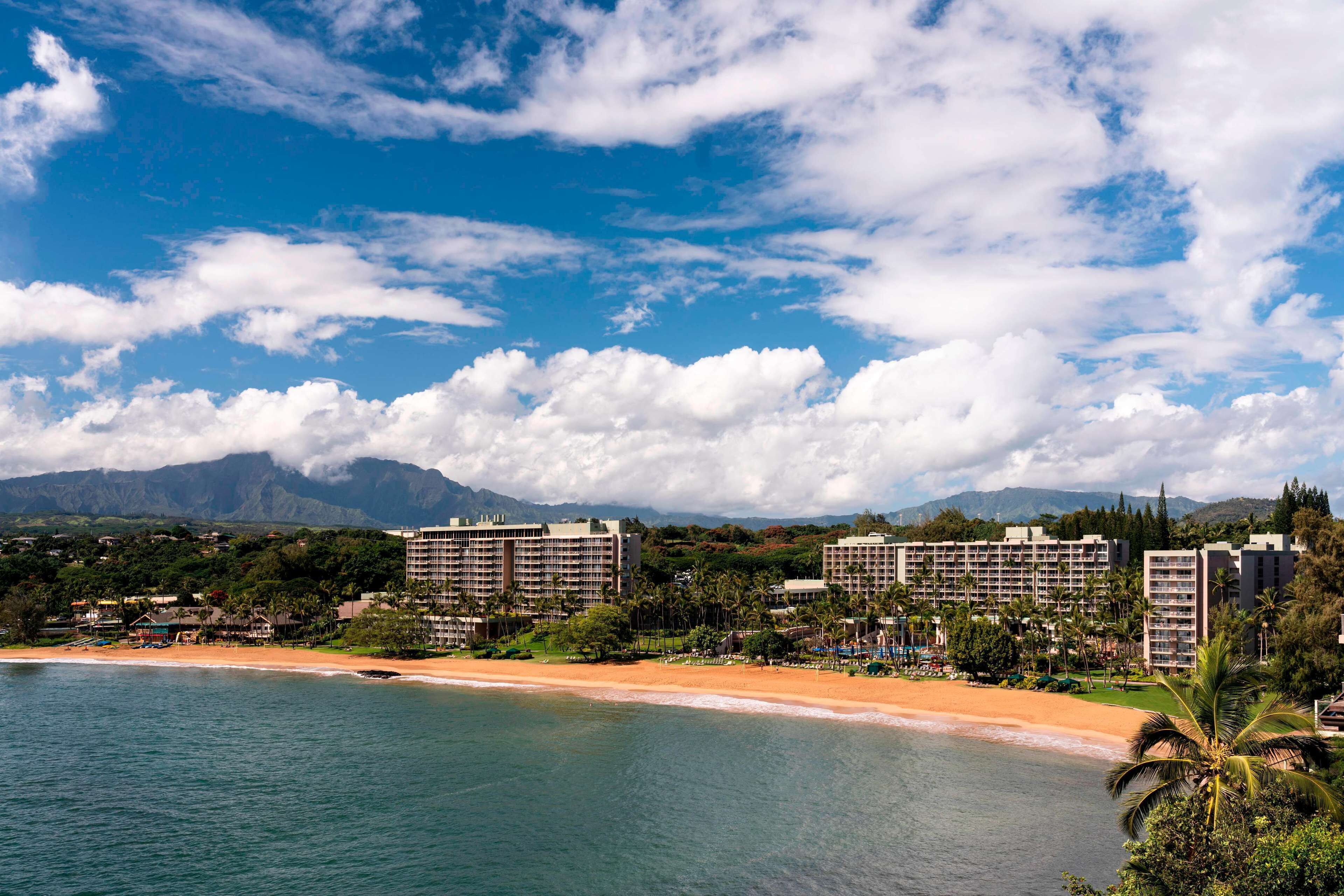 A coastal resort with beachfront hotels, palm trees, and mountains in the background.