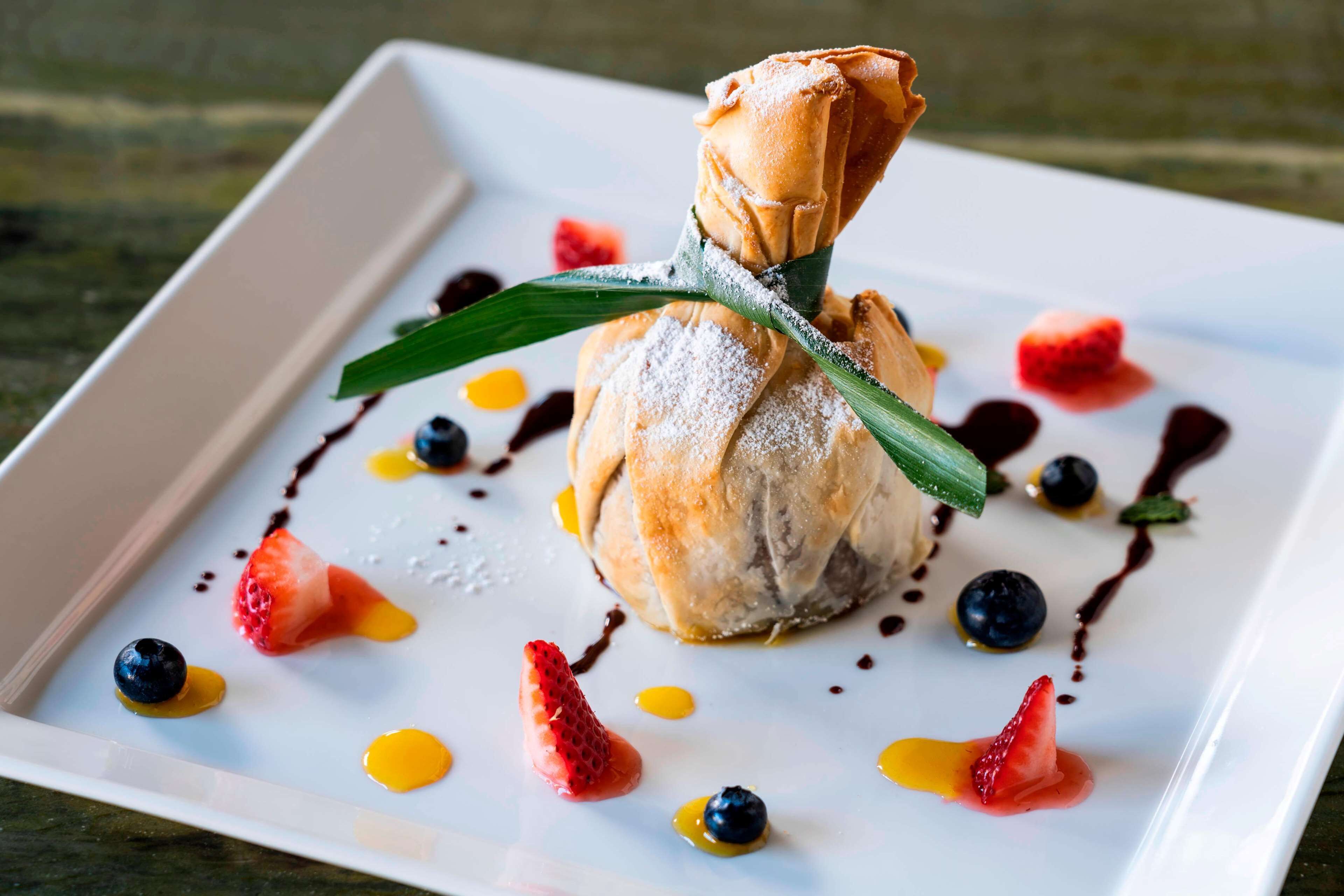 Un plato de postre con un pastel central, fresas, arándanos y salsa de chocolate.