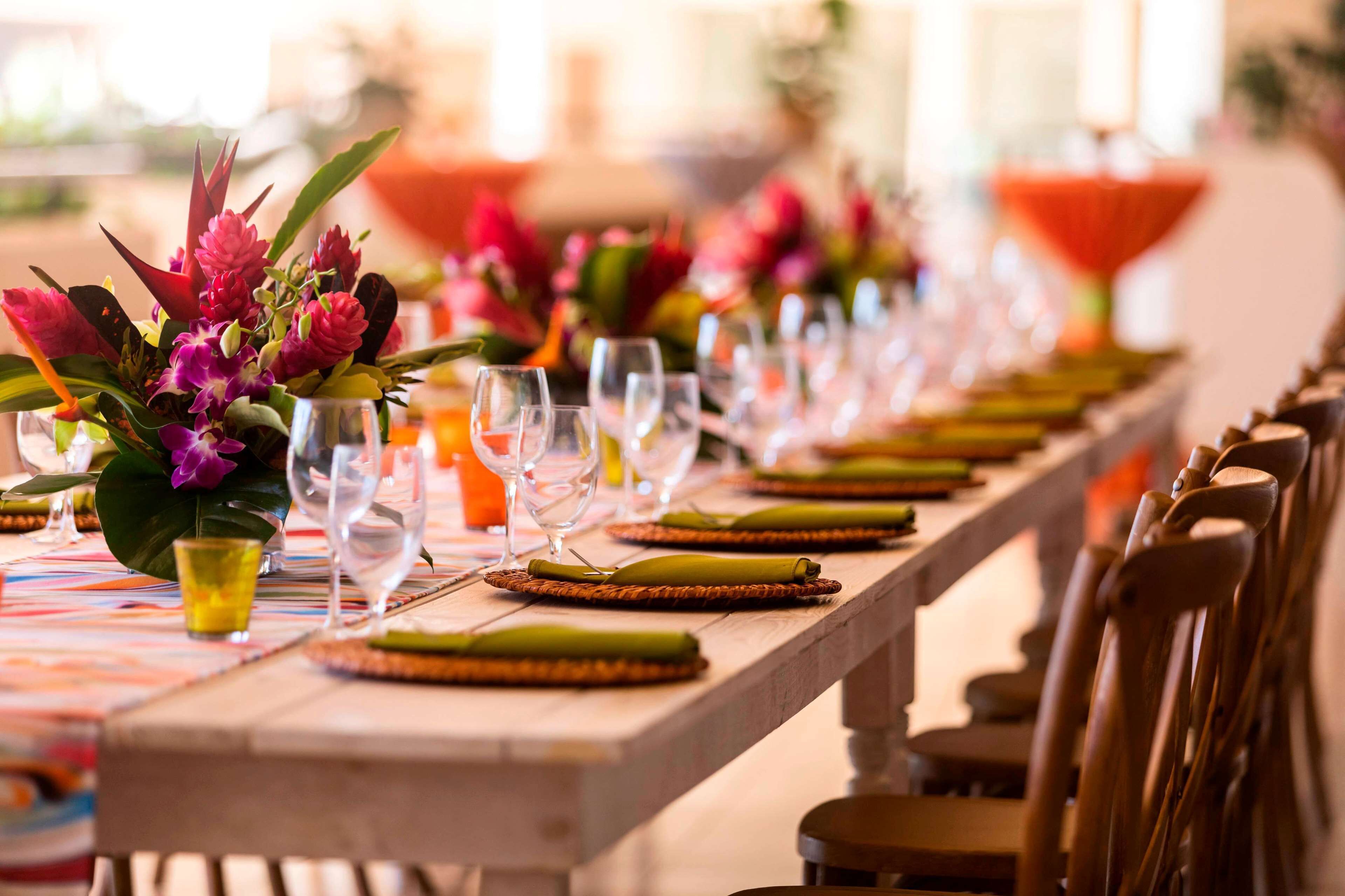 A long dining table set with glassware, green napkins, and a centerpiece of flowers.