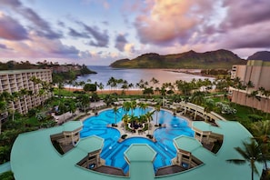Un resort con varias piscinas, una playa y montañas al fondo.