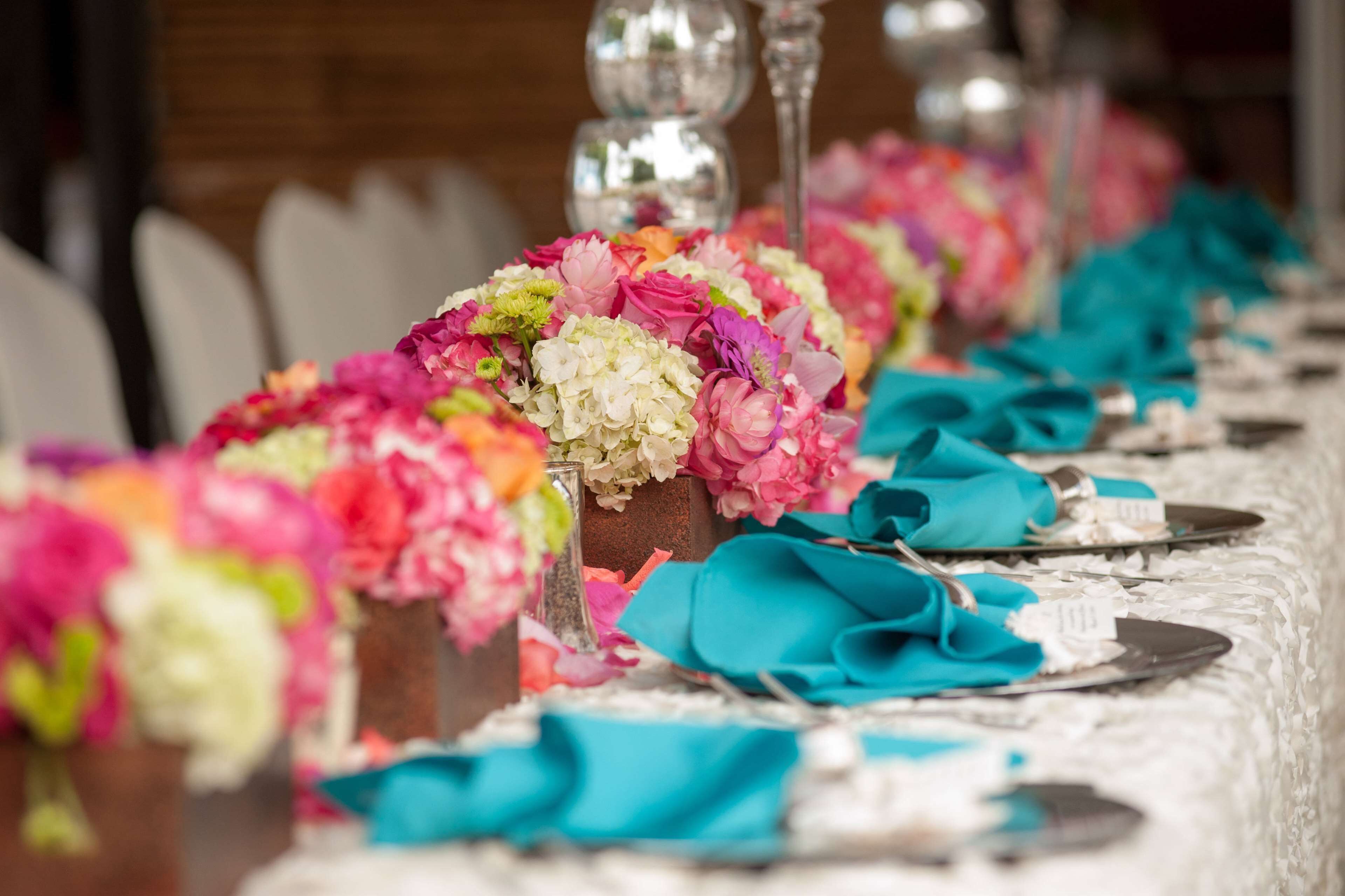 Una mesa adornada con servilletas color turquesa, centros de mesa florales y cubiertos.