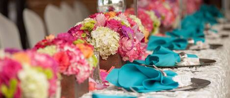 Una mesa adornada con servilletas color turquesa, centros de mesa florales y cubiertos.