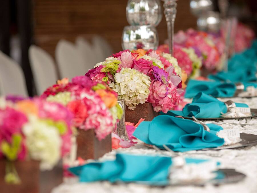 Una mesa adornada con servilletas color turquesa, centros de mesa florales y cubiertos.