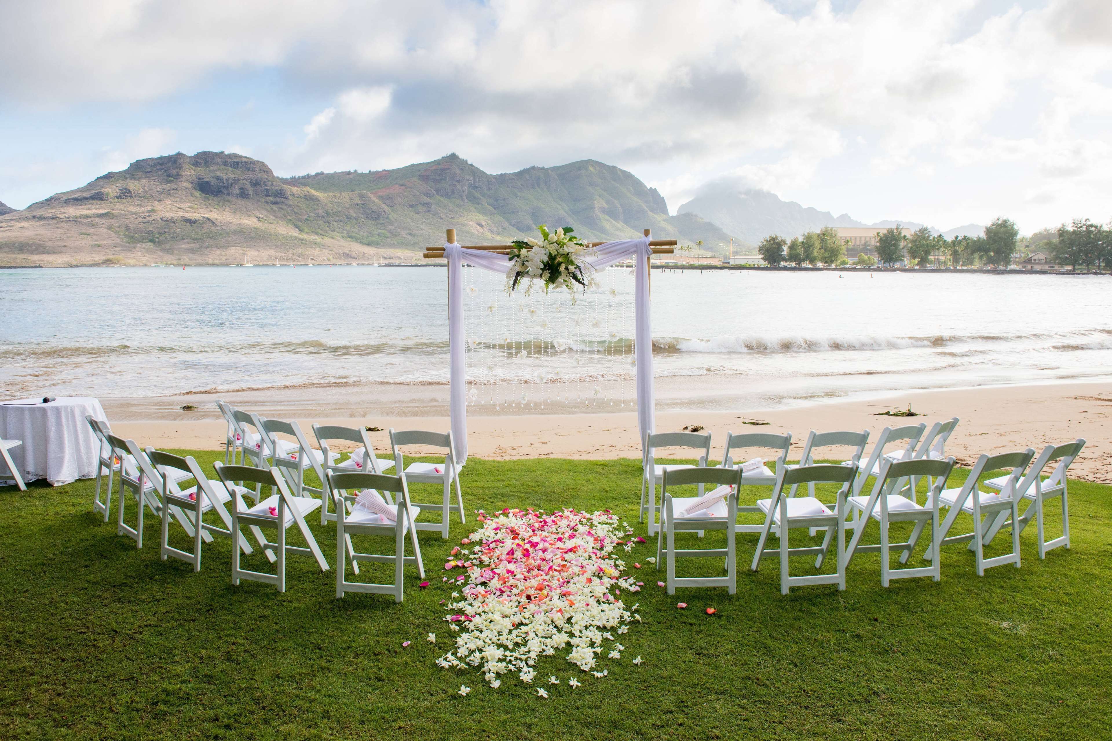 A beach wedding setup with white chairs and a floral aisle.