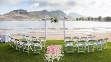 A beach wedding setup with white chairs and a floral aisle.