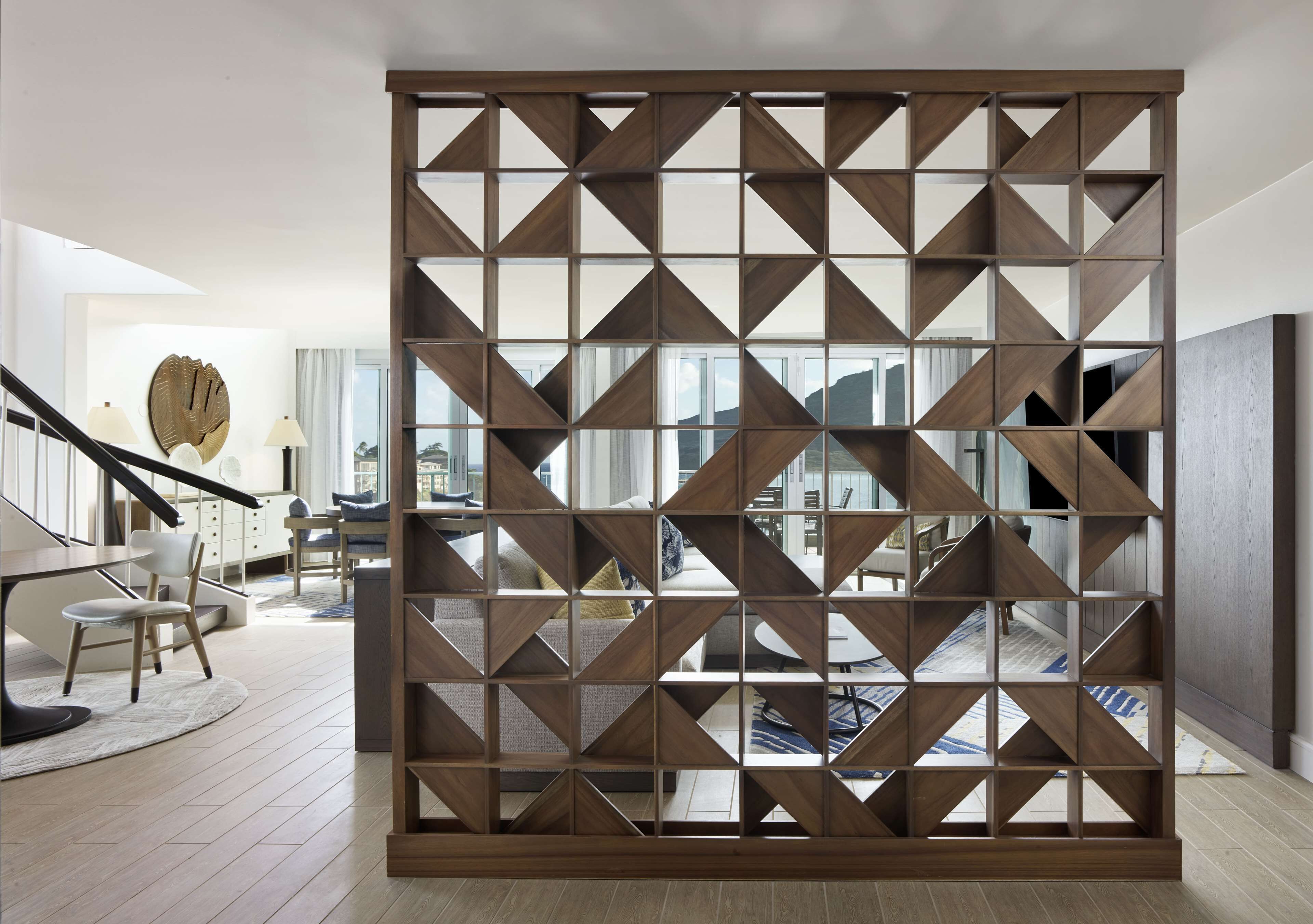 A modern living room with a geometric wooden partition, a staircase, and a view of the city.