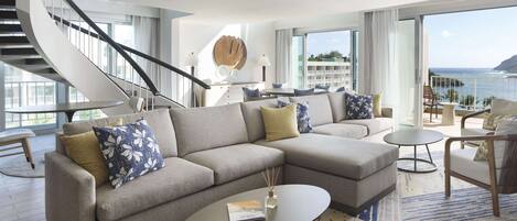 A modern living room with a curved staircase, a sectional sofa, a round coffee table, and a view of the ocean.