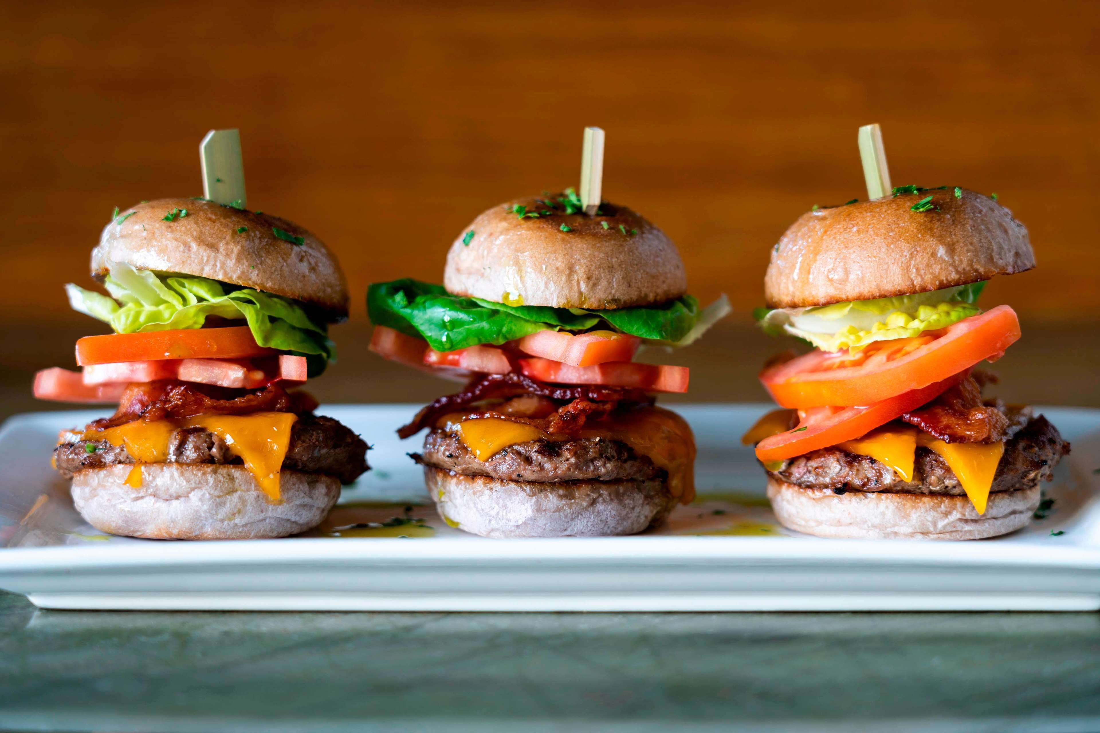Three burgers with various toppings and toothpicks, placed on a white plate.