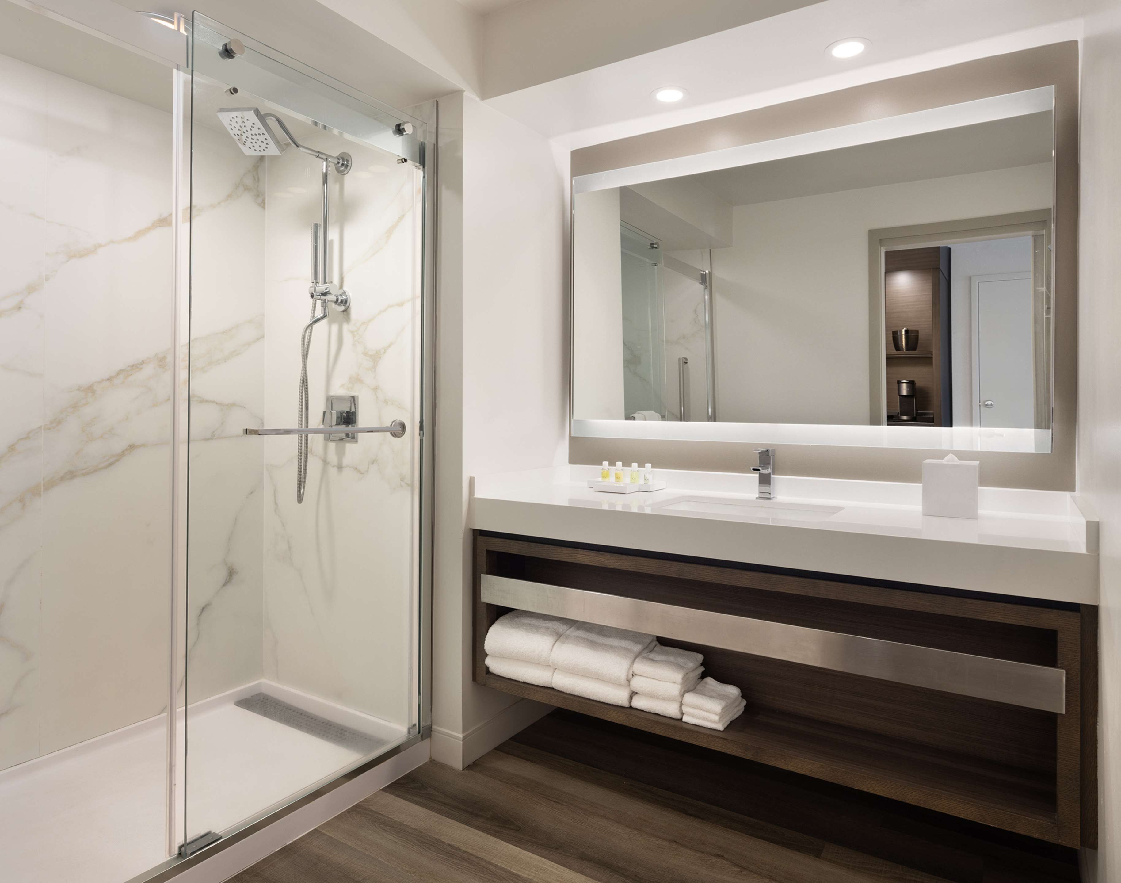 Un baño moderno con ducha envuelta en vidrio, un espejo grande y un tocador con perchero.