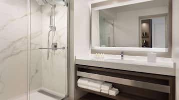 A modern bathroom with a glass-enclosed shower, a large mirror, and a vanity with a towel rack.